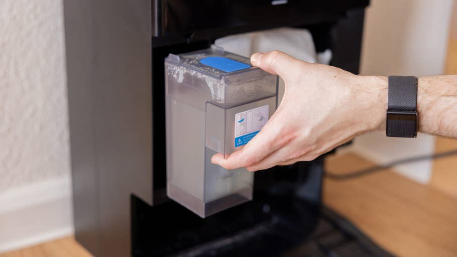 A person removes a water tank from a black device, possibly the Ecovacs Deebot X8 Pro Omni.