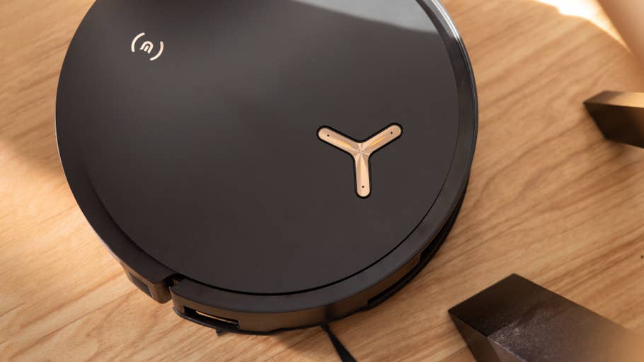 A black, minimalist robot vacuum cleaner on a wooden floor.