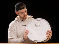 A man in a hoodie examines the ECOVACS N30 Pro Omni robotic vacuum cleaner.