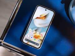 A Google Pixel 9a smartphone displayed on a blue surface next to a blue lamp.