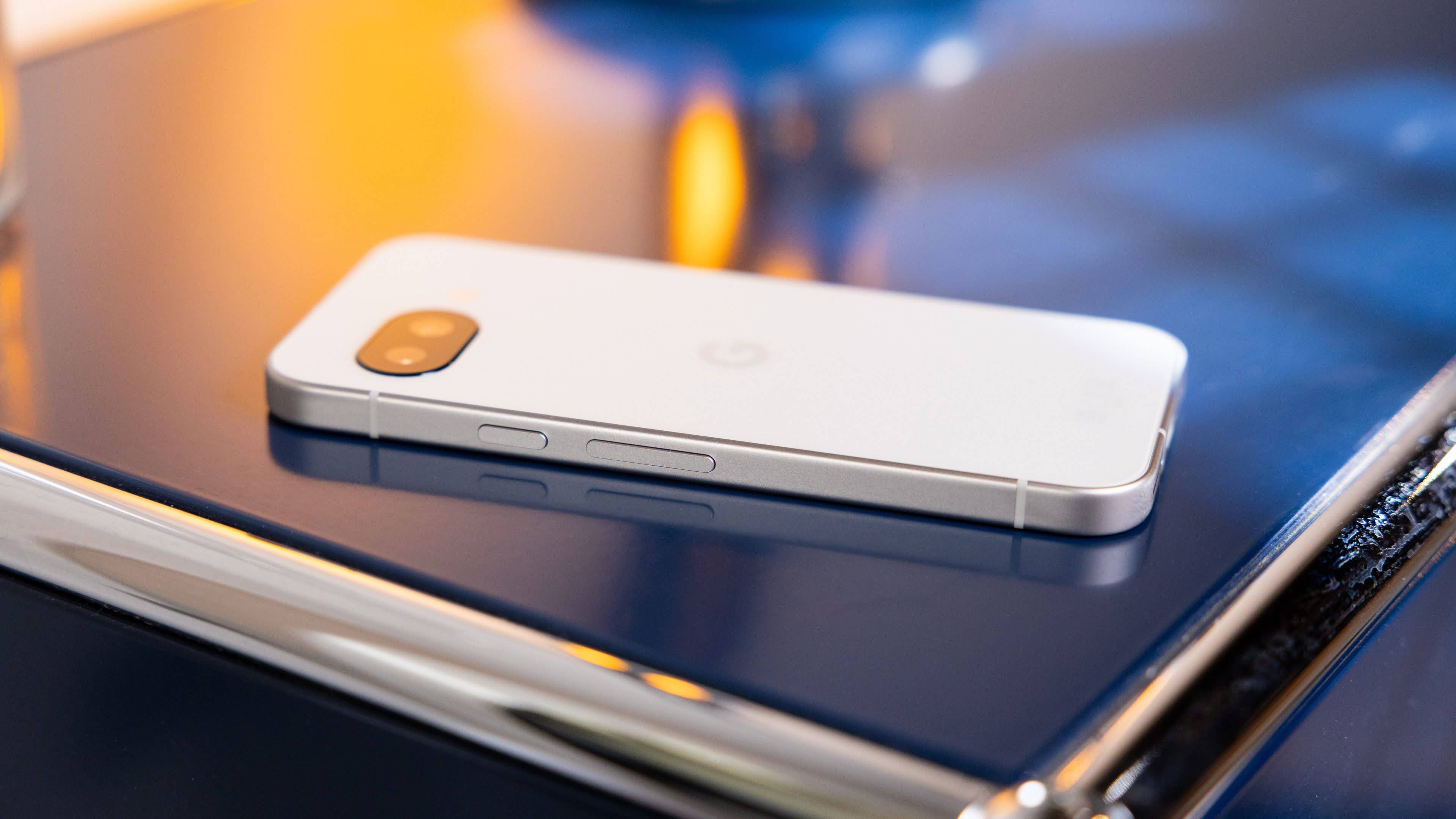 A Google Pixel 9a smartphone lying on a reflective surface with soft lighting.