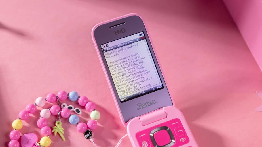 A pink flip phone with the u0027Barbieu0027 logo and text displayed on the screen, next to colorful beads.