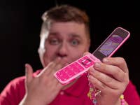 nextpit_HMD_Barbie_Phone_Test.jpg A person in a red shirt holds a pink Barbie phone with a colorful screen, playfully covering their mouth.