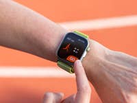 A person holds a smartphone displaying a 5K training plan with performance metrics on a running track.