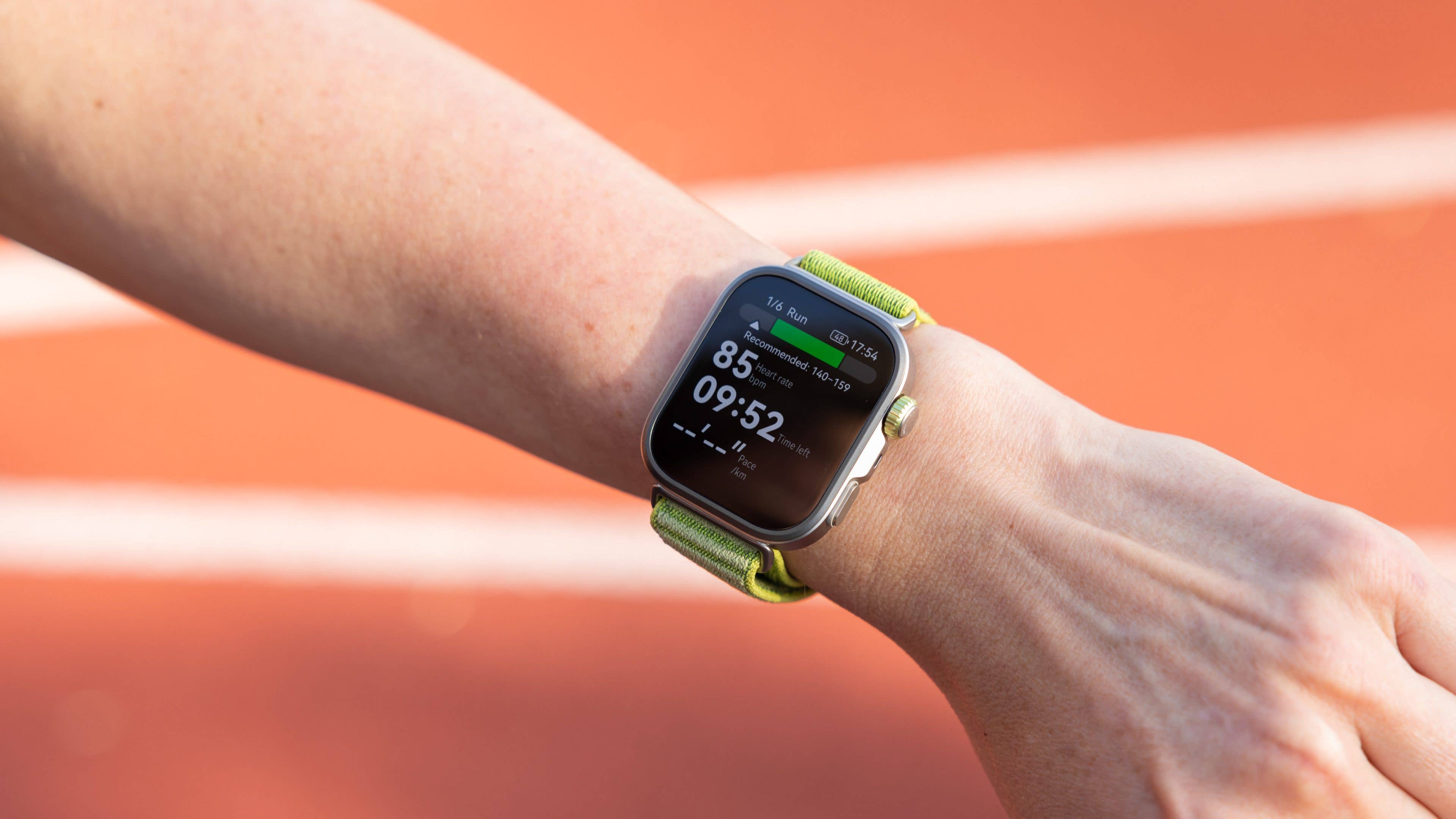 A person holds a smartphone displaying a 5K training plan with performance metrics on a running track.
