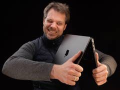 A man laughing while holding a MacBook Pro in front of a black background.