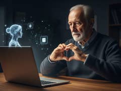 An elderly man makes a heart shape with his hands while looking at a laptop displaying a holographic AI figure.