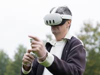 A man wearing a virtual reality headset outdoors, holding a controller and pointing.