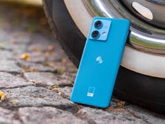 A Motorola Edge 40 Neo smartphone leaning against a tire on cobblestone pavement.