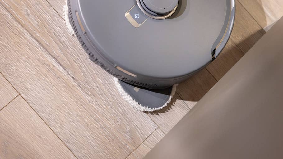 A robot vacuum cleaner on a wooden floor, partially hidden behind a wall.