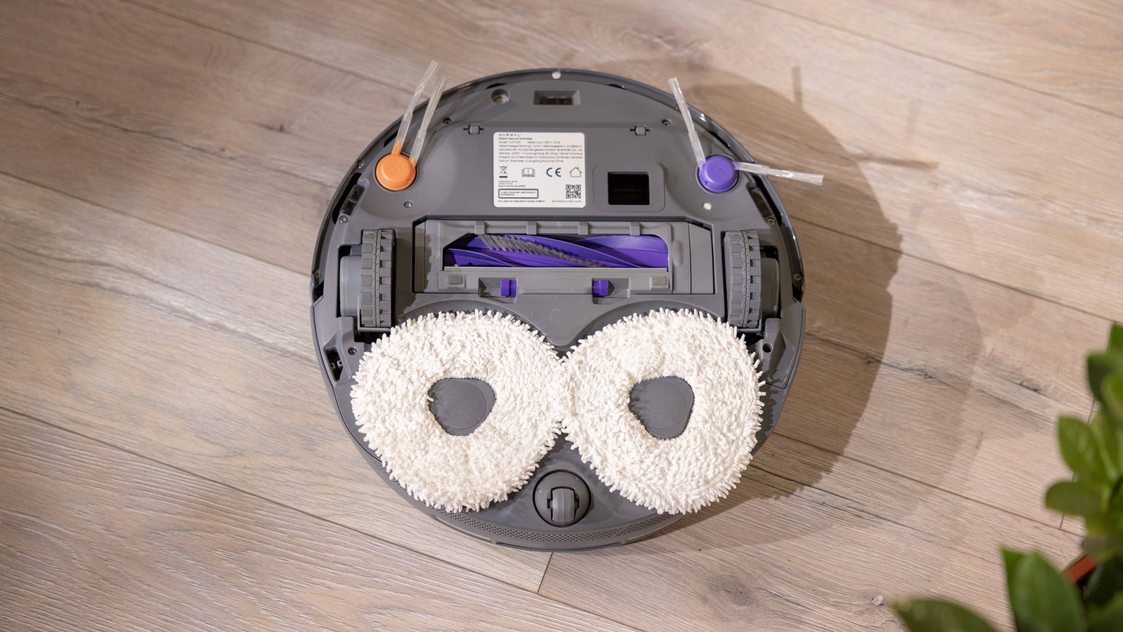 A robotic vacuum cleaner with two round mop pads on a wooden floor.