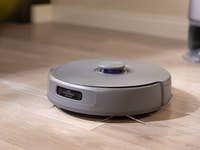 A gray robotic vacuum cleaner on wooden floor.