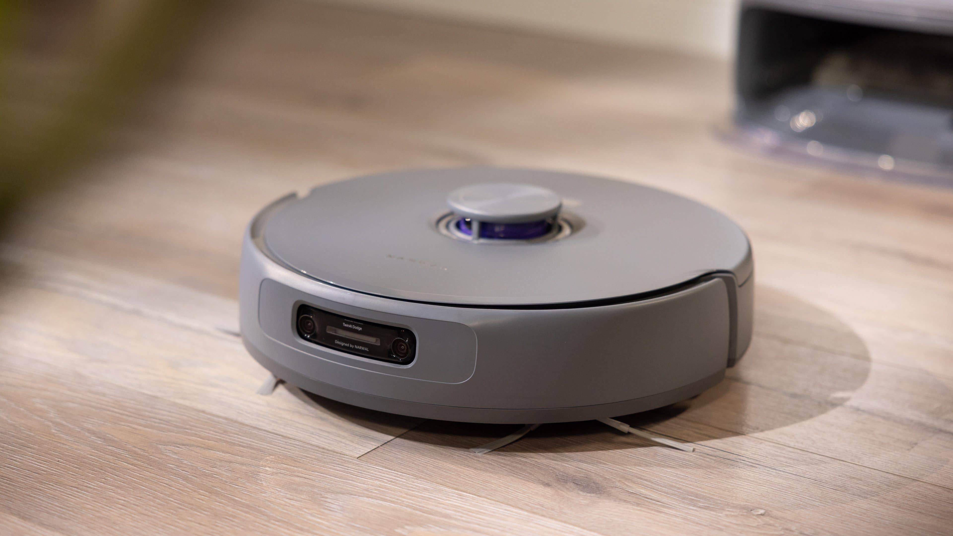 A round gray robotic vacuum cleaner on a wooden floor.