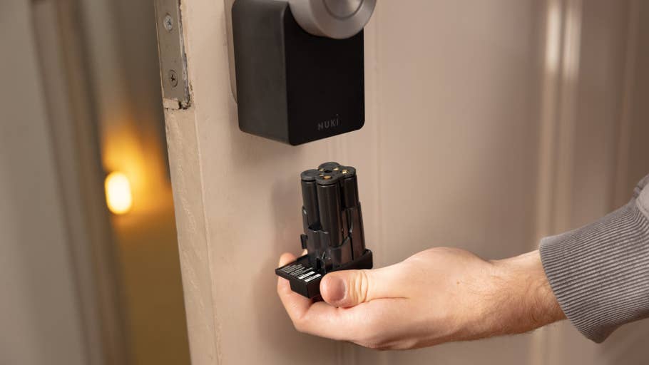A person holds the Nuki Smart Lock Pro while standing next to a door where the lock is installed.