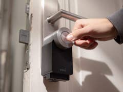 A hand operating a Nuki smart lock on a door.