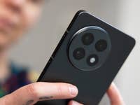 A person holds a OnePlus 13R smartphone displaying its rear camera design.