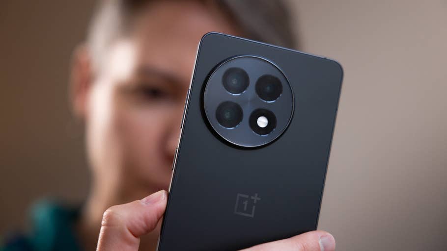 A close-up of a OnePlus 13R smartphone being held by a person, showing its rear camera design.