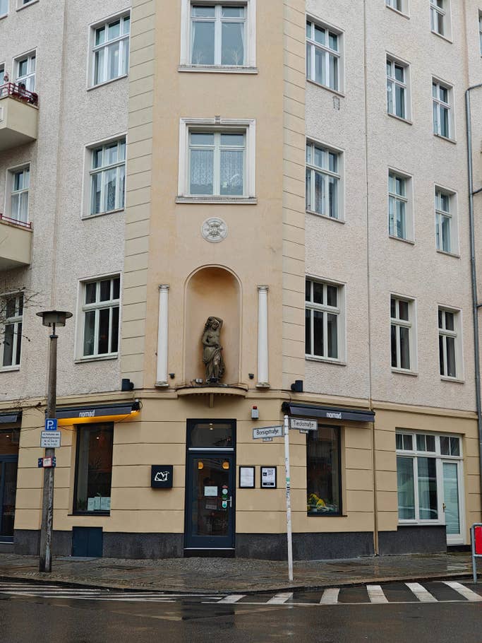A building corner with an ornate statue, large windows, and a sign for u0027nomadu0027 cafe.