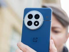 A person holding the blue back of a OnePlus 13 smartphone, showcasing its camera design.