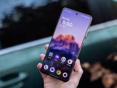 A person holding a OnePlus 13 smartphone with a colorful home screen showing the time 15:50.