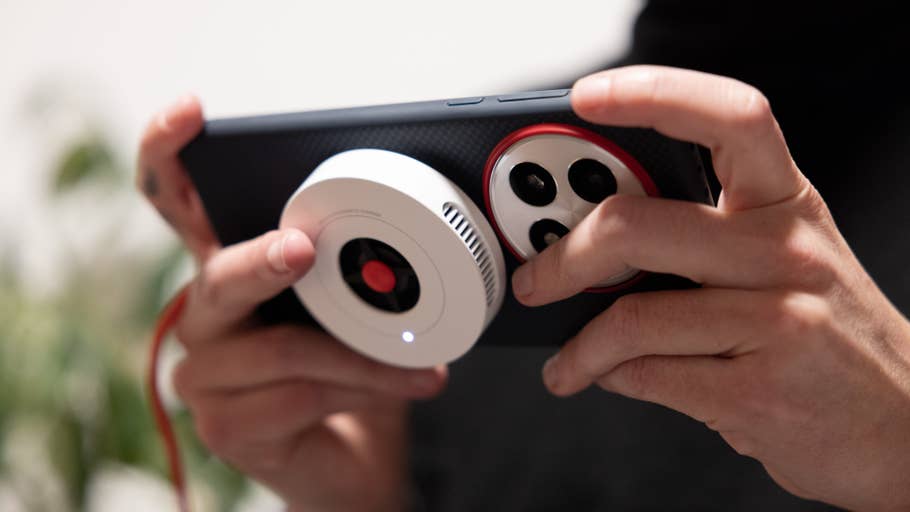 A person holding a OnePlus 13 smartphone with a camera attachment.