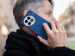 A person with short gray hair is using a OnePlus 13 phone while talking on the street.
