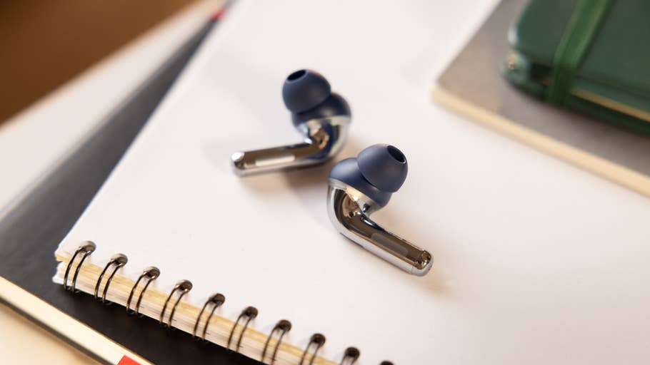 The OnePlus Buds Pro 3 wireless earbuds placed on a closed green notebook and planner.