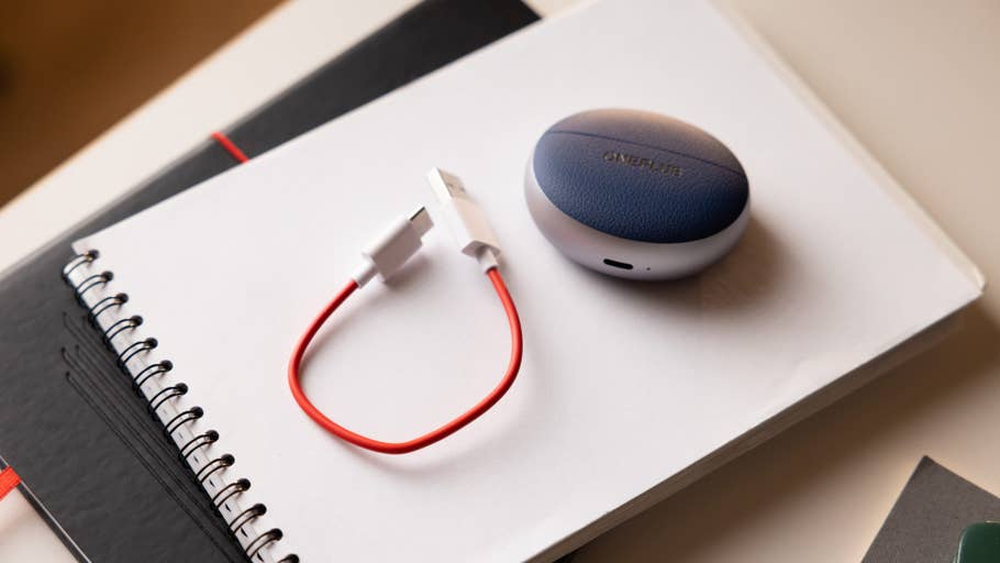 The OnePlus Buds Pro 3 charging case with a red USB cable on a notebook.