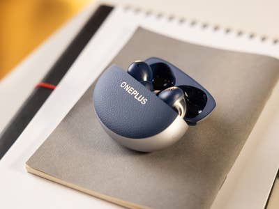 The OnePlus Buds Pro 3 charging case on a notebook with a pencil.