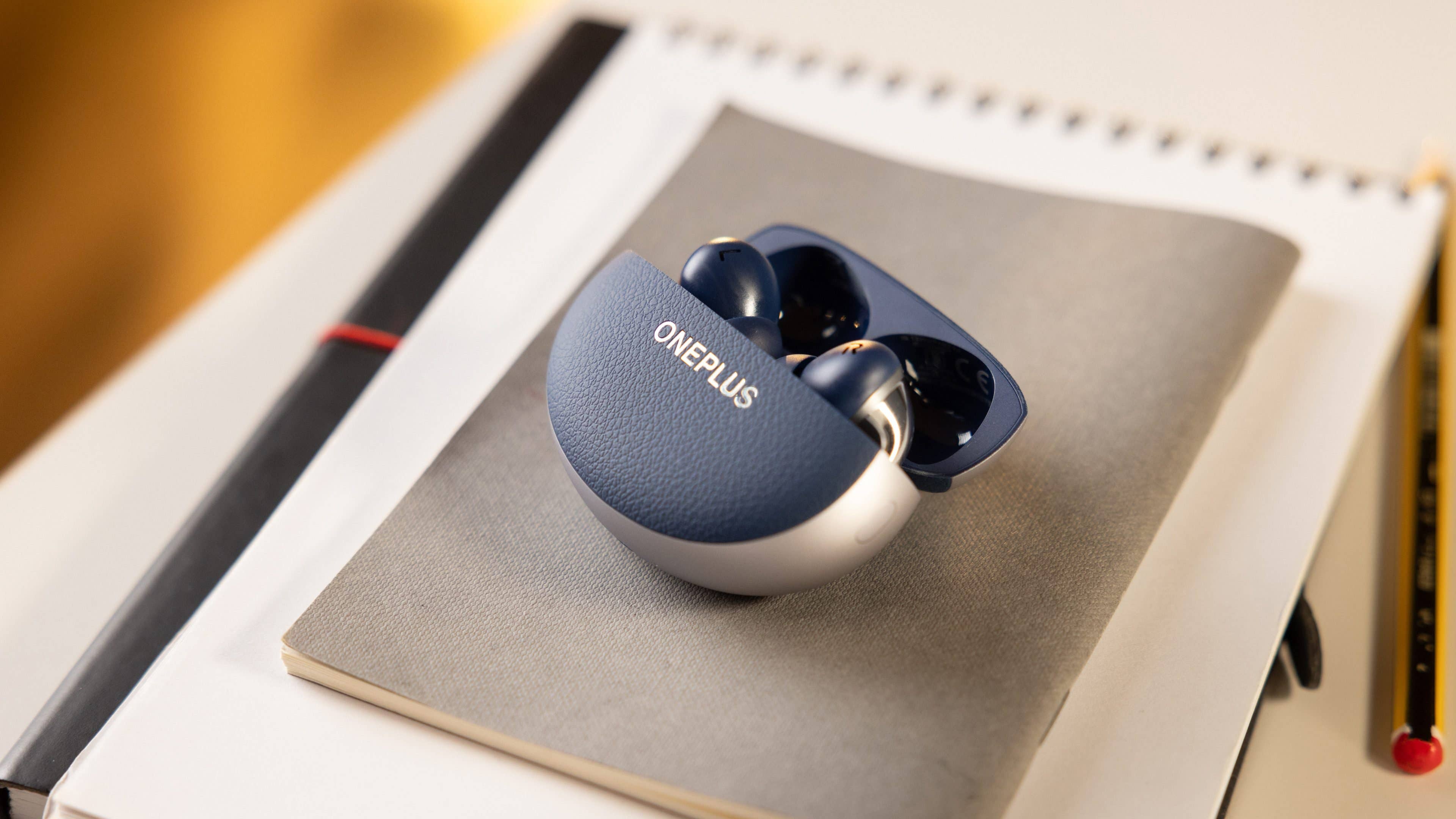 OnePlus Buds Pro 3 charging case on a notebook with a pencil.