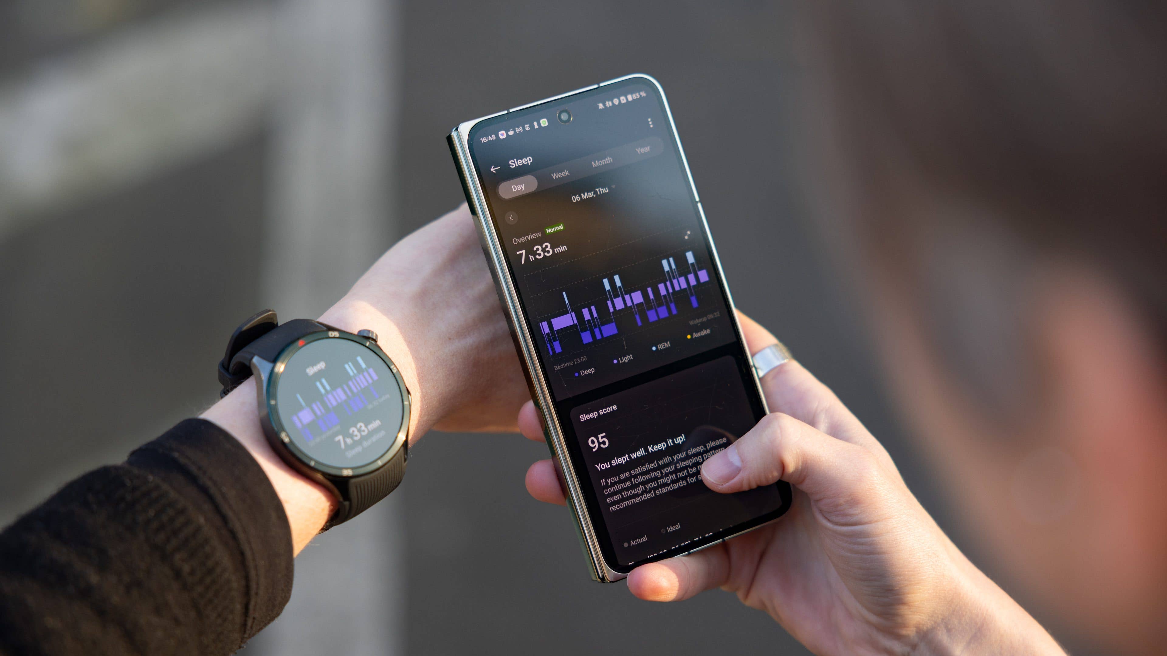 A person checking sleep data on a smartphone while wearing a OnePlus watch on their wrist.