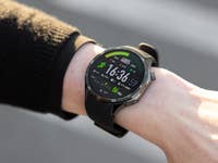 A wrist displaying a OnePlus Watch 3 with a green and black digital interface showing time and fitness stats.