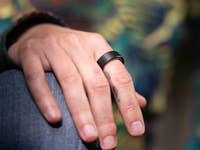 A close-up of a hand wearing a black Oura Ring 4 on the finger, resting on a knee.