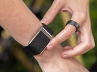 A person adjusting an Oura Ring on their wrist, wearing a black mesh band and a simple black ring.