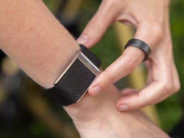 A person adjusting an Oura Ring on their wrist, wearing a black mesh band and a simple black ring.