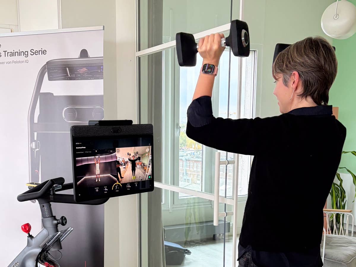 Testing Peloton IQ in action: the new Cross Training Bike+ uses computer vision to track form and provide real-time feedback during strength workouts. A person lifting weights in front of a Peloton display for cross training.