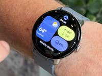 A close-up of a Google Pixel Watch 4 displaying weather information for Berlin, showing 64°F and mostly cloudy.