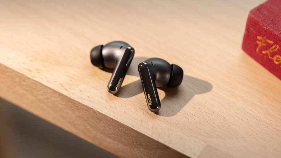 Redmiu0027s black Buds 6 Pro rest on a wooden surface next to a red book.