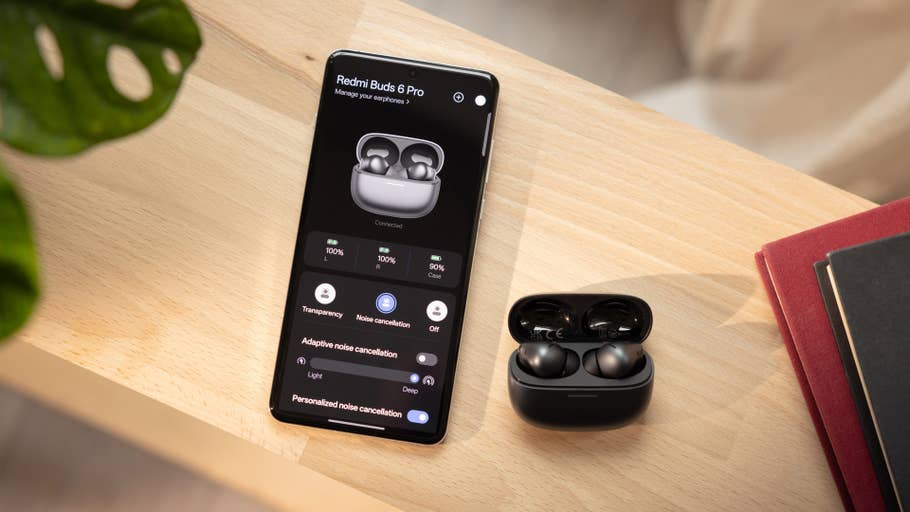 Redmi Buds 6 Pro displayed on a phone screen with the earbuds case is on a wooden surface.