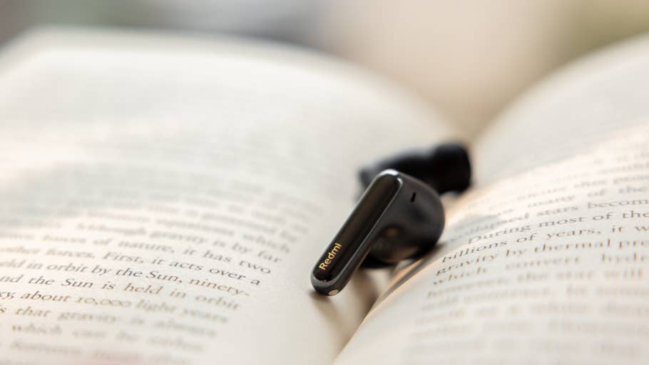 A Redmi Buds 6 Pro wireless earbud lies on an open book page.