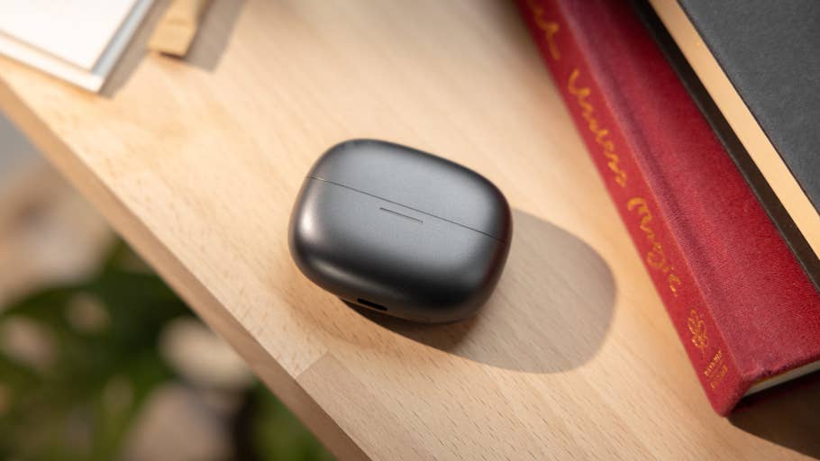 Close-up of a black charging case for Redmi Buds 6 Pro on a wooden surface next to books.
