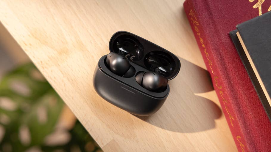 Black wireless earbuds in charging case on wooden surface next to books.