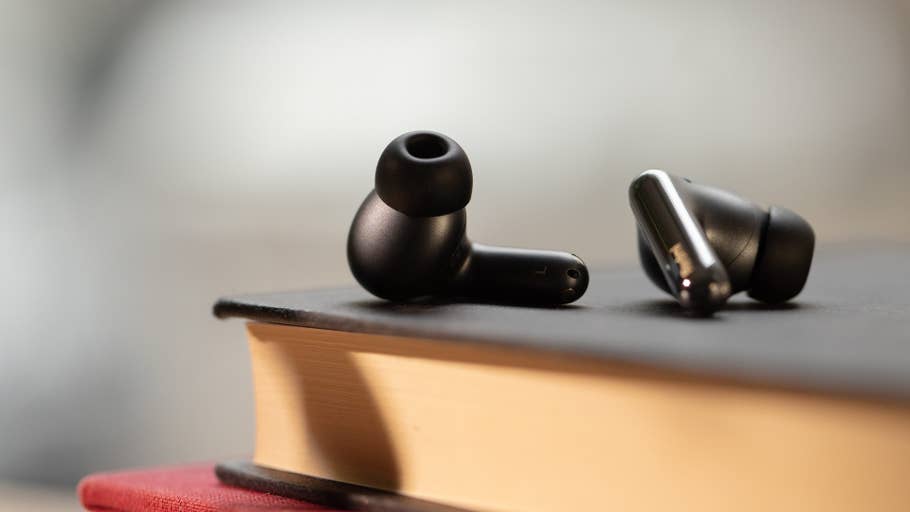 A pair of black Redmi Buds 6 Pro earbuds resting on a book.