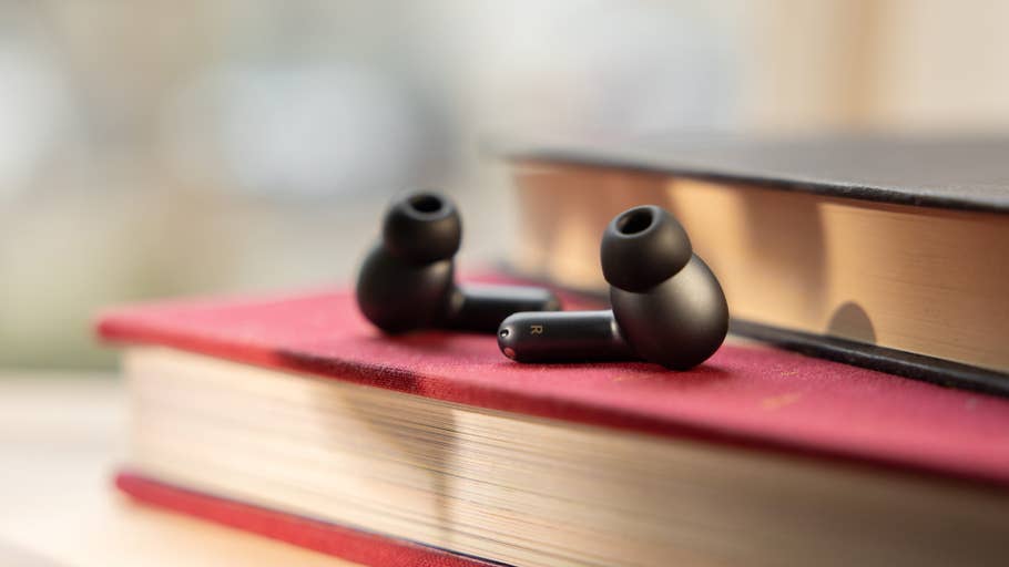 Black wireless earbuds resting on a red book, with a blurred background.