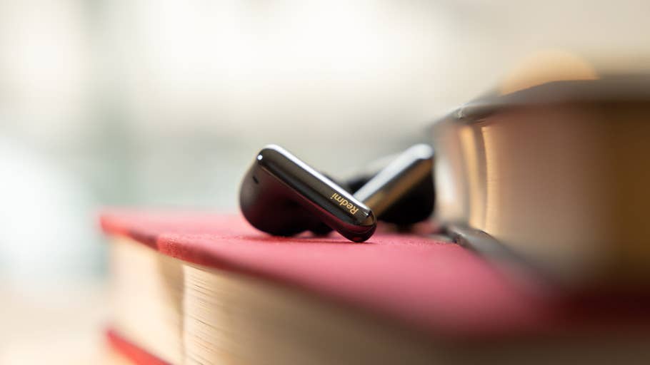 Black Redmi Buds 6 Pro resting on a red book with a blurred background.