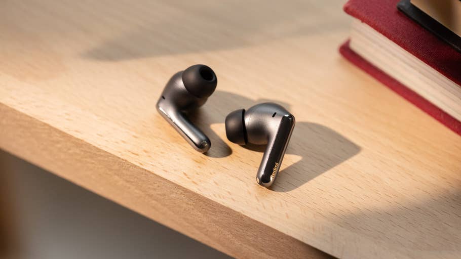 Black wireless earbuds on a wooden surface next to books.