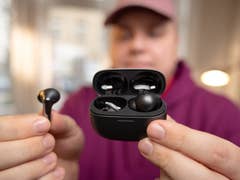 A person holding a black case with wireless earbuds, one earbud is being held separately.