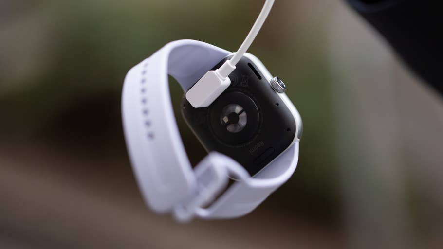 A Redmi Watch 5 charging with a white strap and visible magnetic connector.