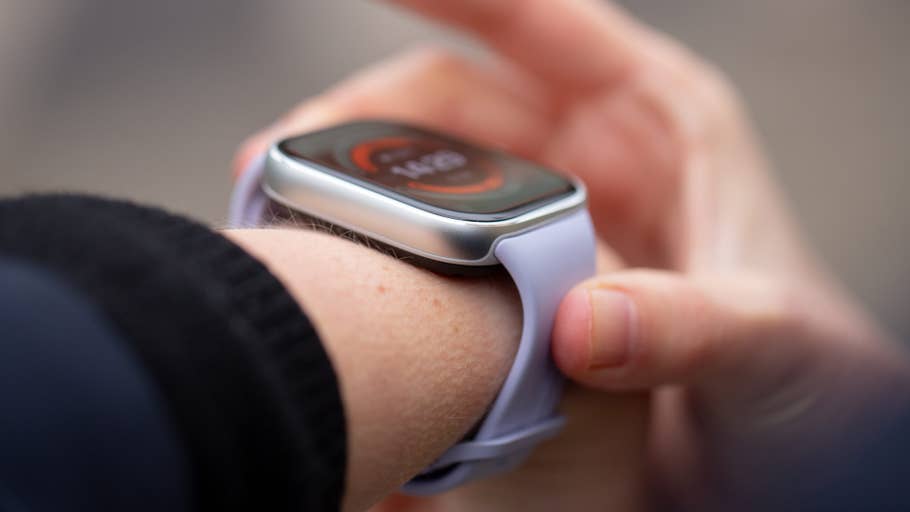 A person adjusting a Redmi Watch 5 on their wrist, displaying the time on its screen.