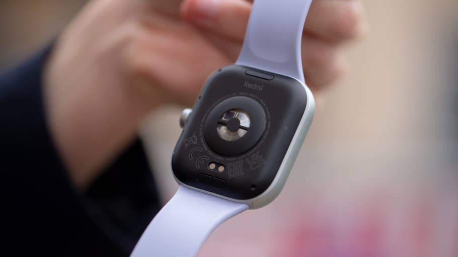 A person holding a Redmi Watch 5, showing the back with sensors and a white strap.